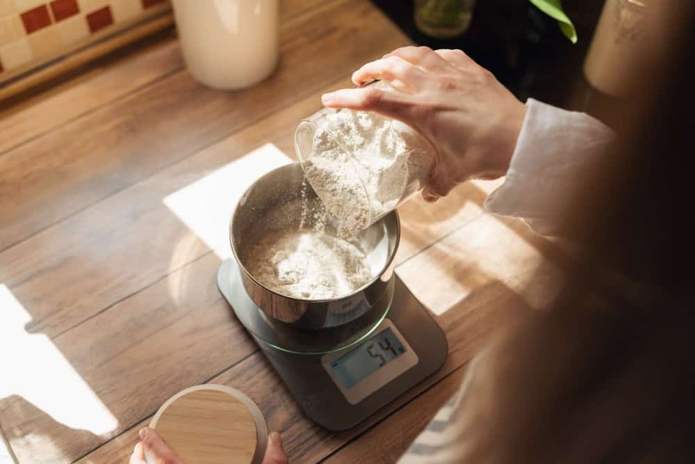A digital kitchen scale measuring flour in a bowl for accuracy.