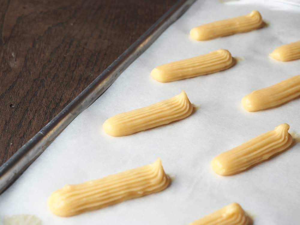 A baker piping éclairs in straight, even lines onto a baking tray