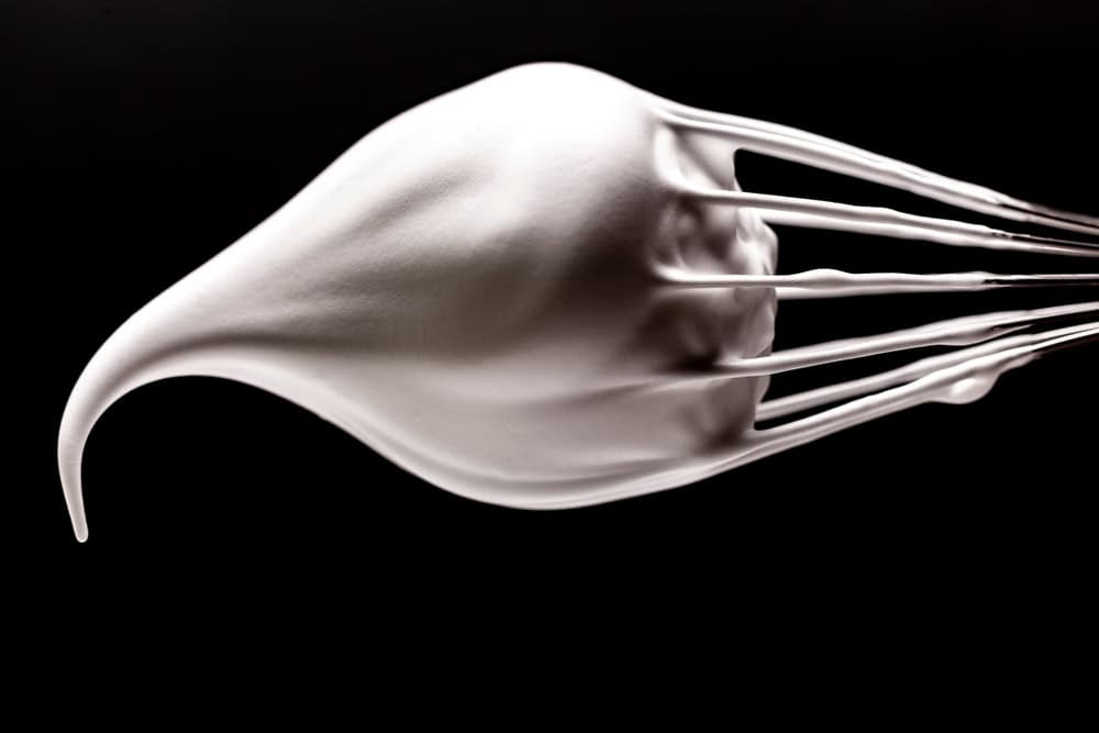 A bowl of egg whites whipped to medium peaks, with glossy and slightly soft tips.