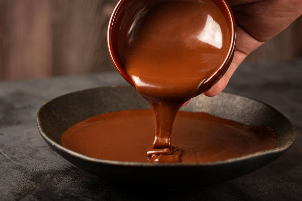A bowl of glossy chocolate ganache being mixed for éclair glaze